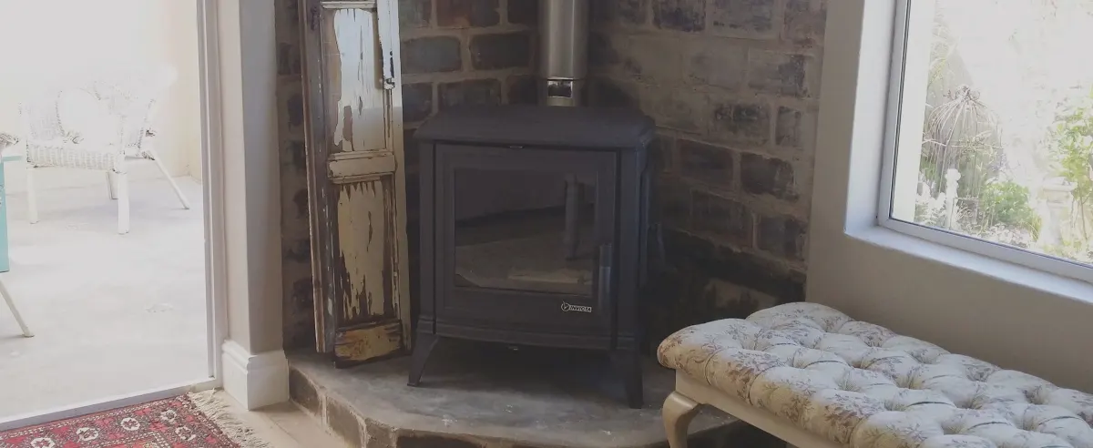 Black freestanding wood-burning stove installed into a stone corner recess in a Cape home