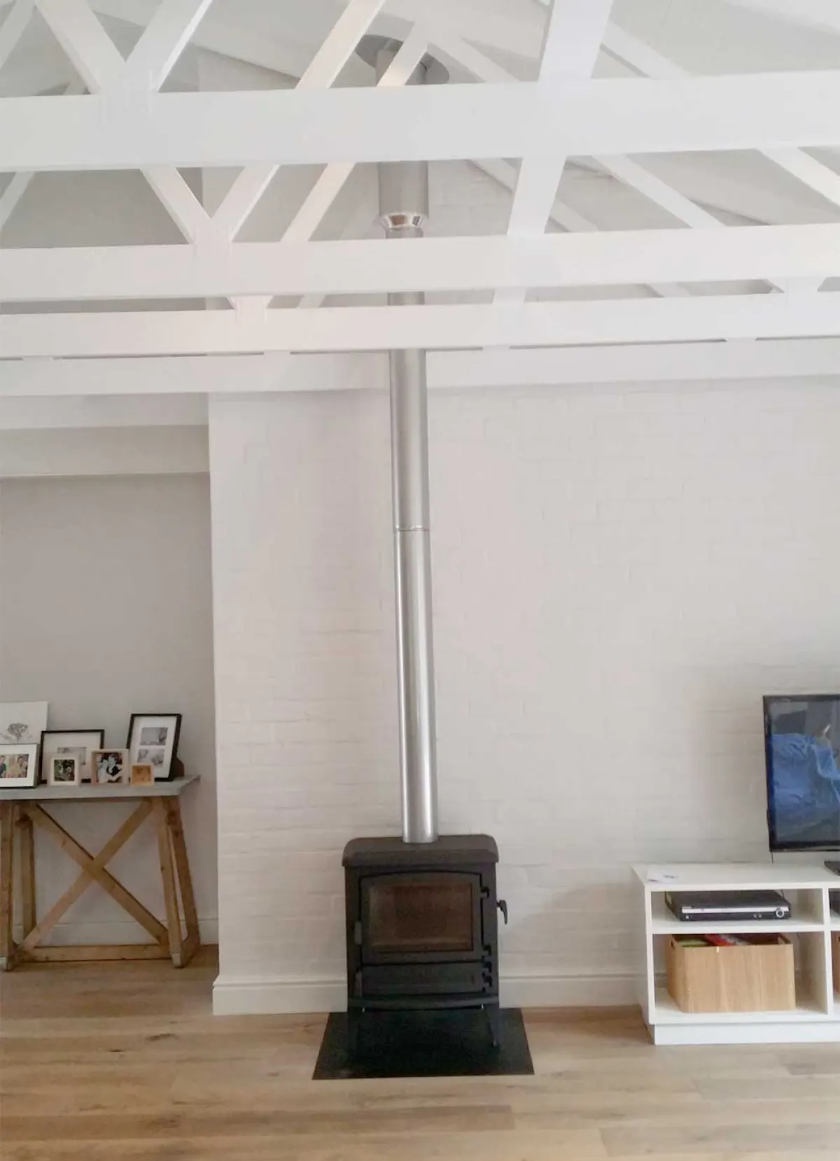 Compact wood stove with a stainless flue in a white room with exposed roof beams