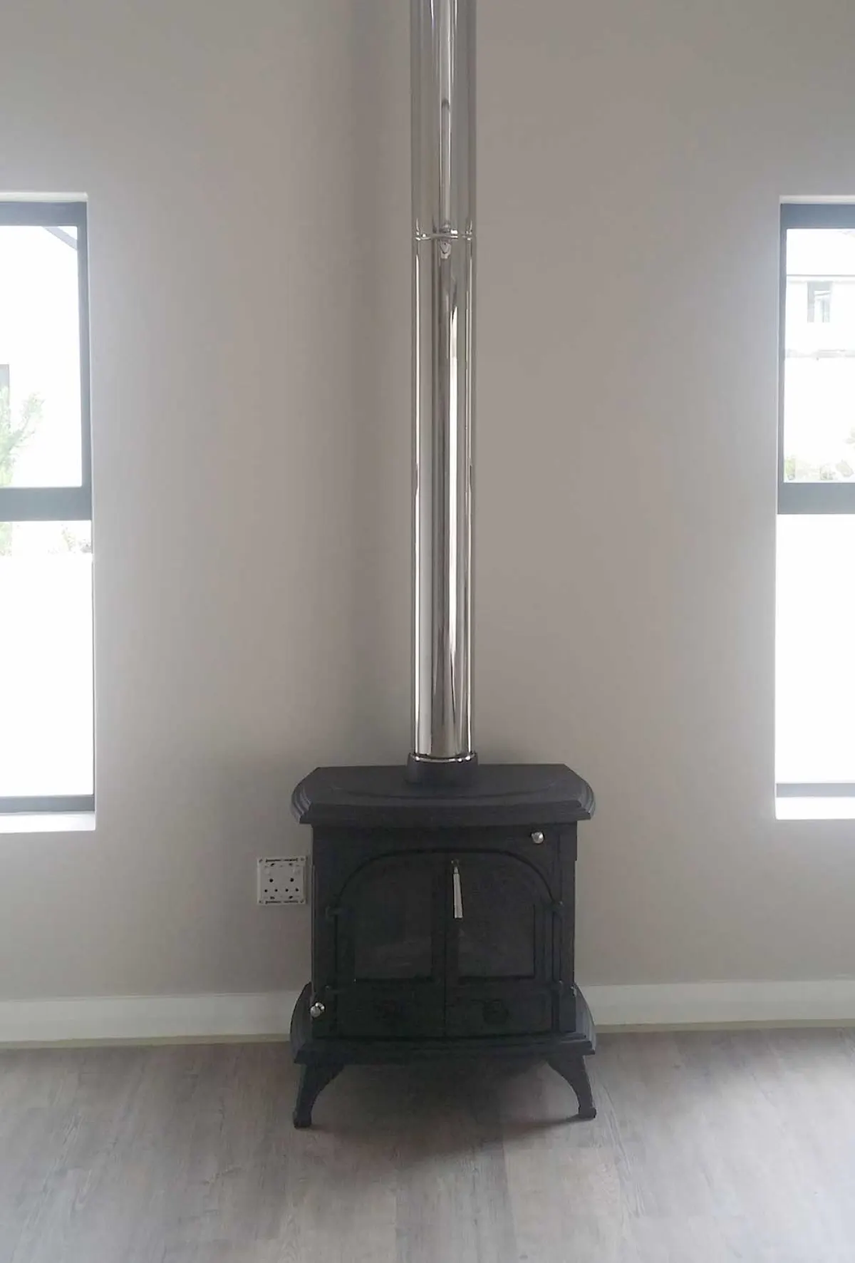 Small cast-iron stove installed in the corner of a lounge with the flue run to the ceiling