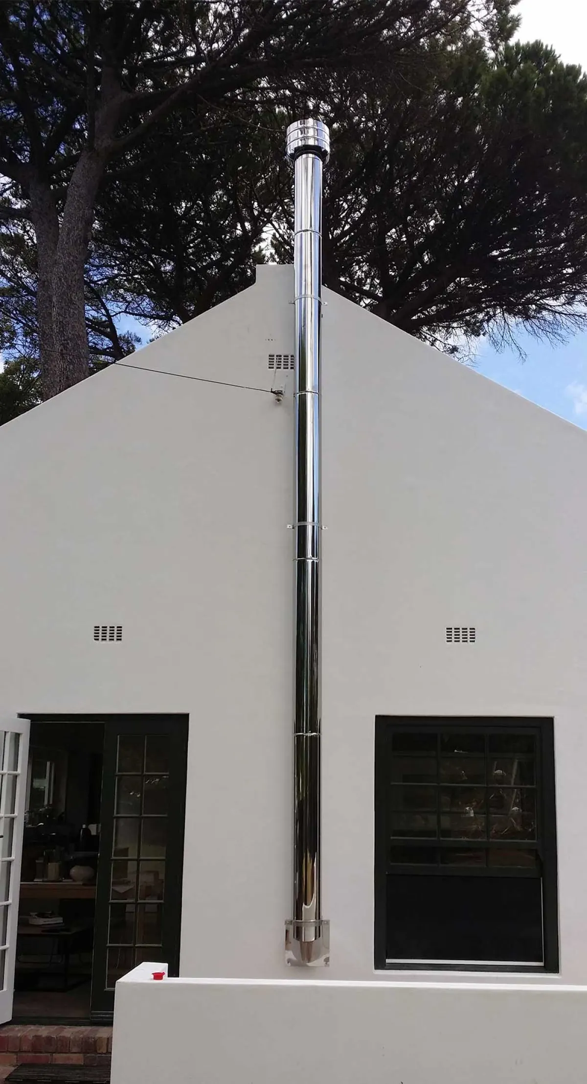 Polished stainless steel flue running up the exterior gable of a white Cape house
