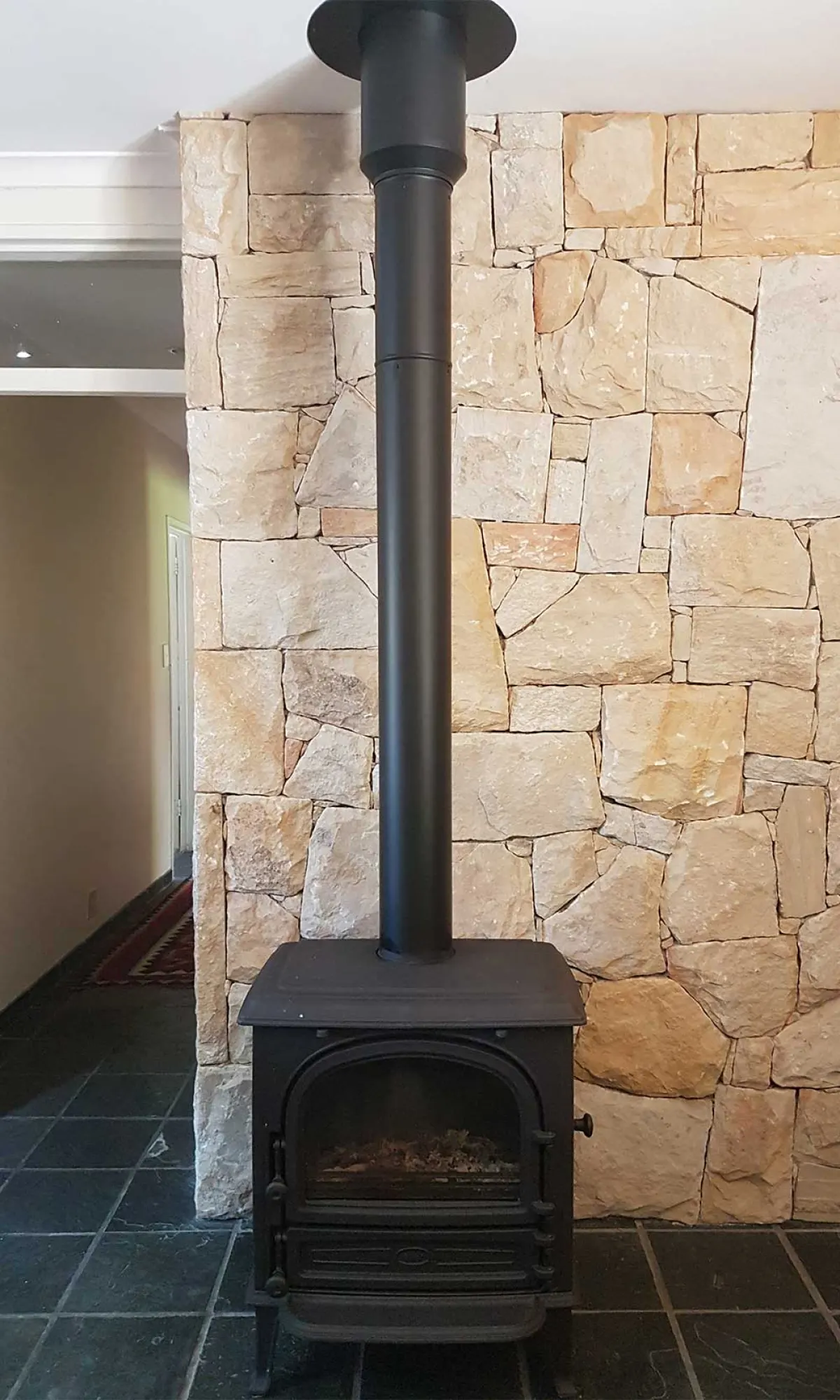 Freestanding stove against a stone-clad wall with a black flue running to the ceiling