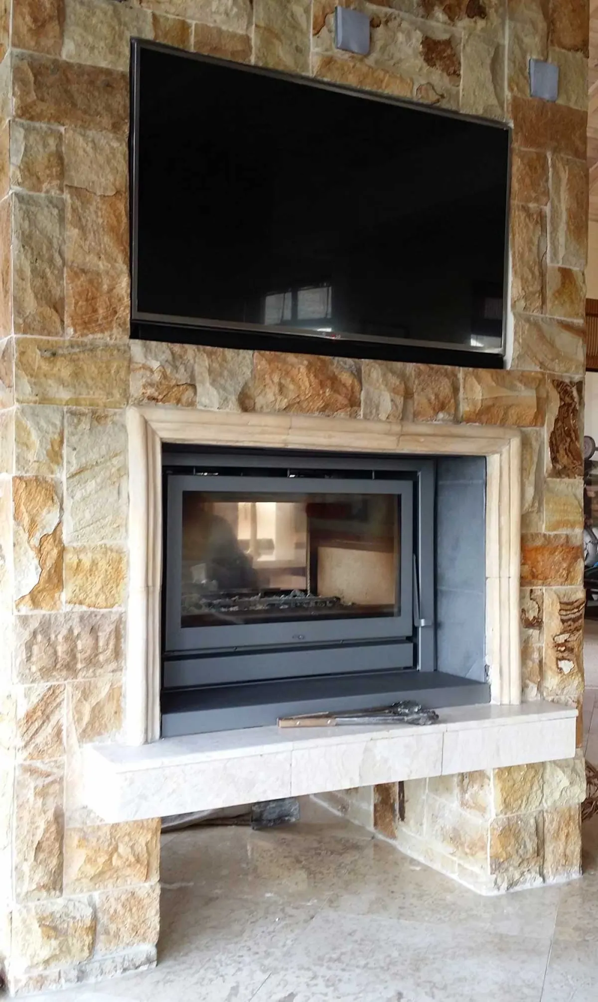 Fireplace insert built into a rough stone feature wall below a wall-mounted television